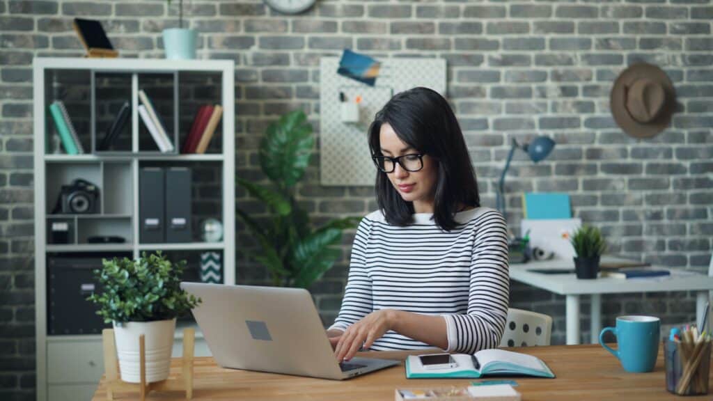 woman at her desk on laptop with white striped top looking at the benefits of market intelligence