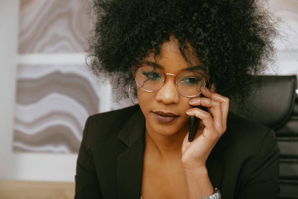 Woman on her desk at work is on the phone and looks worried as she experienced a lack of communication from her colleagues which is a clear sign of silo mentality.