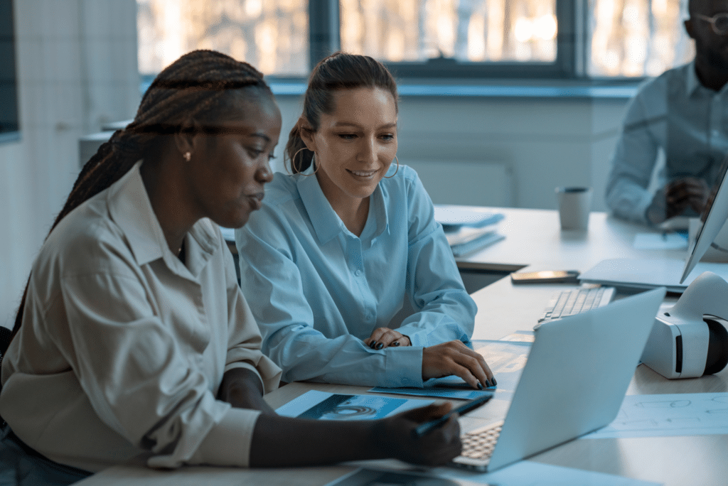 Two women at a laptop in a meeting room look at AI-powered insights 