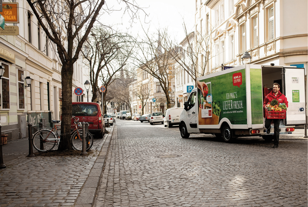 REWE Group delivery vehicle with worker unloading fresh produce.