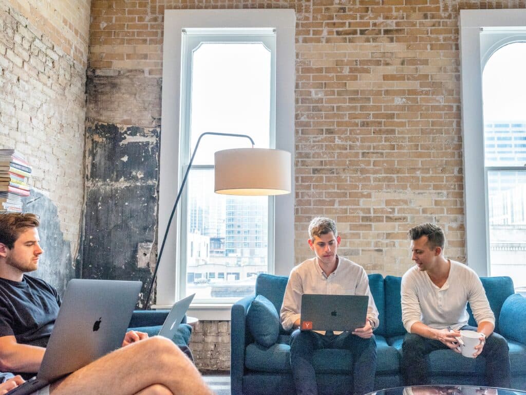 men with laptops sitting on blue couches researching market research vs consumer insights