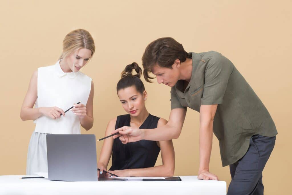 One man and two women on a laptop with orange background look at AI in knowledge management solutions