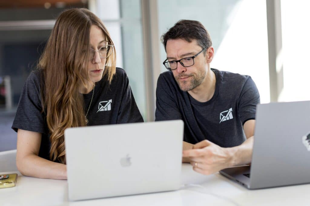 Two co w-orkers, a man and woman in black t-shirts on their laptops analyzing AI-powered insights