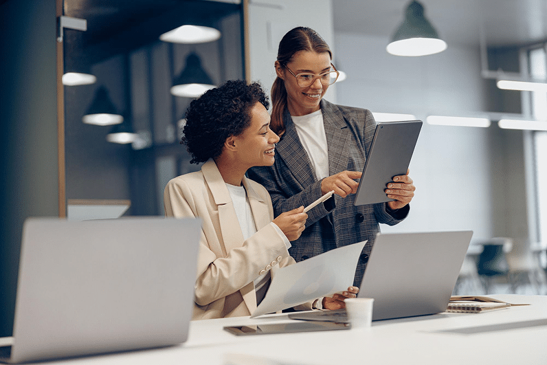 Two colleagues discussing insights using a tablet and laptops in an office setting