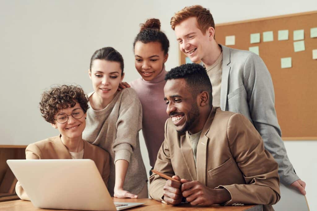 a team of five people smile around a desk, they represent a team who works together to eliminate redundant data