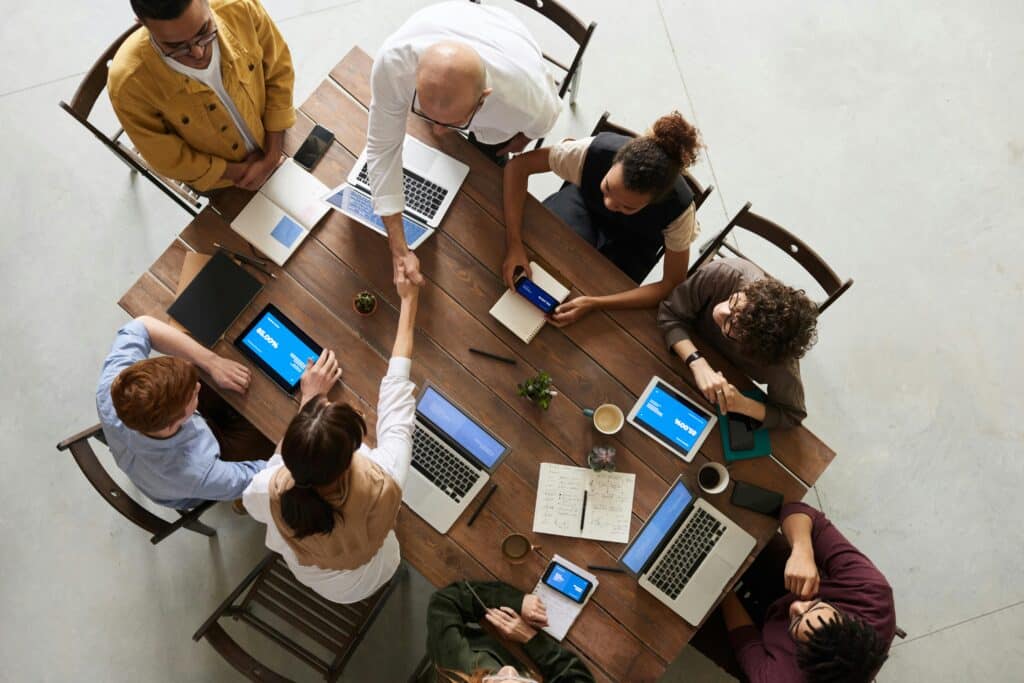 Group of eight colleagues around a table with laptops and ipads discuss AI change management and how it is the result of collaboration