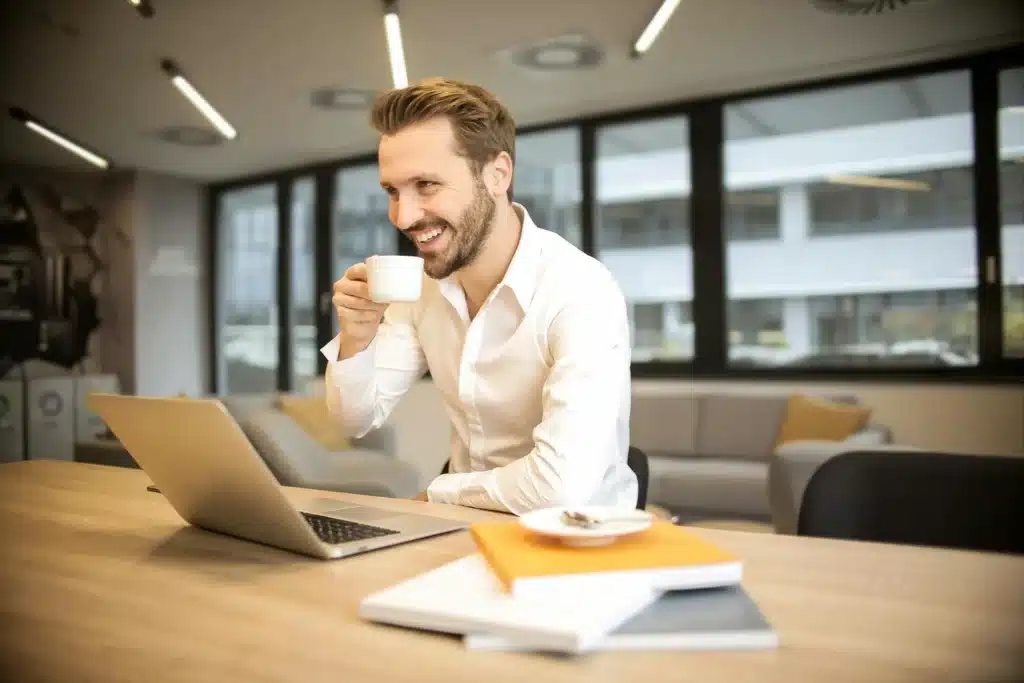 man at his desk smiling at a laptop in a white shirt, as he has a positive experience working with market intelligence to make sense of customer experience data